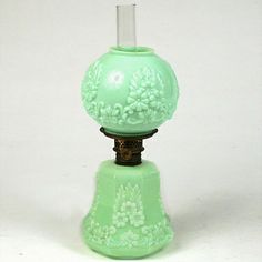 a green glass lamp with flowers on it's base and a white background behind it