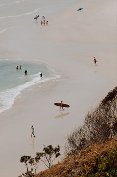 people are walking on the beach with surfboards