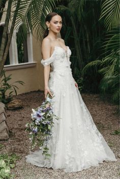 a woman in a white wedding dress holding a flower bouquet and posing for the camera