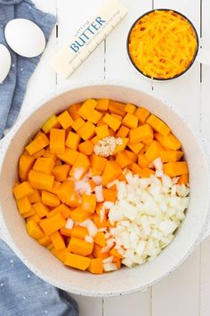 a bowl filled with chopped up vegetables next to an egg and butter shaker on a white table