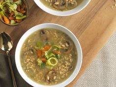 two bowls of mushroom soup on a cutting board with spoons and utensils