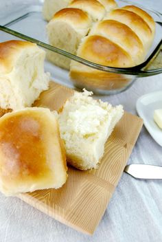 rolls and butter on a cutting board next to a glass dish full of buttered bread