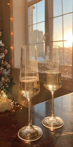 two wine glasses sitting on top of a table next to a christmas tree in front of a window