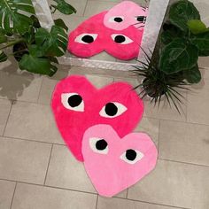 two pink heart shaped rugs with eyes on the floor next to a potted plant