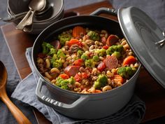 a large pot filled with lots of food on top of a wooden table next to utensils