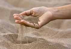 a person holding sand in their hand on top of some sand covered ground and grass