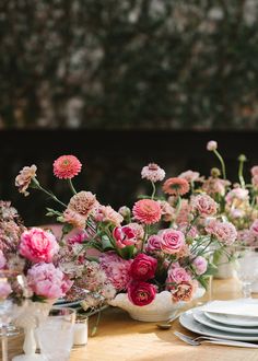 a table topped with lots of pink and white flowers next to plates on top of a wooden table