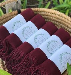 four rolls of wine colored linens in a wicker basket with greenery around them