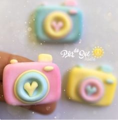 three miniature cameras are sitting on the finger of someone's hand, one is pink and blue