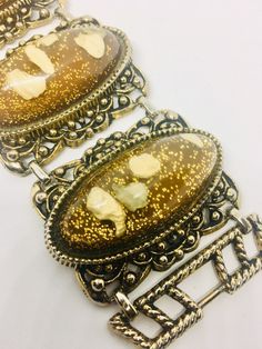 Fabulous vintage extra wide Lucite confetti glitter bracelet with imbedded pebbles. Long lucite cabochons set in ornate antiqued gold tone metal settings. Brown/copper and gold glitter color perfect for fall. Bracelet is in excellent vintage condition with minimal age appropriate wear... if any. It measures 7 1/2 inches long by 2 inches wide. Clasp secure.   Thanks for looking. Antique Jeweled Gold Bracelets, Gold Metal Bracelets With Cabochon, Gold Metal Bracelet With Cabochon, Unique Gold Collectible Bracelets, Vintage Resin Jewelry For Party, Vintage Resin Jewelry For Parties, Ornate Gold Bracelets For Collectors, Gold Decorative Metal Jewelry, Vintage Jeweled Gold Bracelets