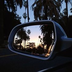 palm trees are seen in the reflection of a car's side view mirror at sunset