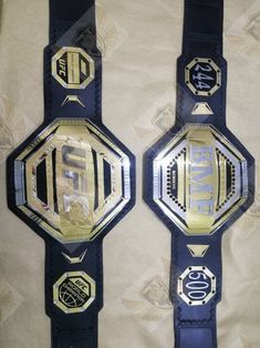 two wrestling belts with gold and black designs on the sides, one for each wrestler