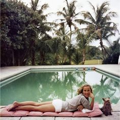 a woman laying on top of a towel next to a swimming pool with a dog