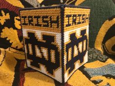 a knitted box sitting on top of a yellow and black blanket covered in designs