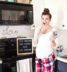 a woman is standing in the kitchen brushing her teeth with an ice cream bar and smiling at the camera