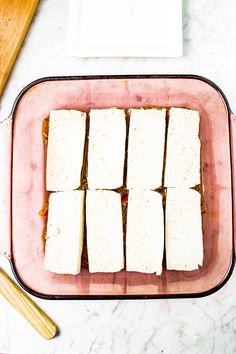 tofu cubes in a glass dish with chopsticks on the table next to it