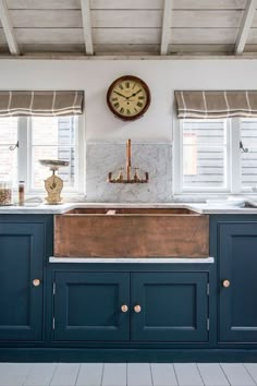 a kitchen with blue cabinets and a large clock on the wall above the sink in front of it