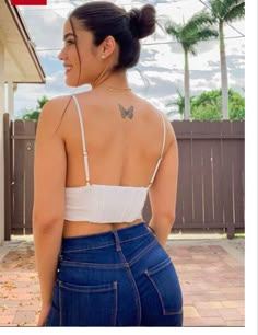 a woman with a butterfly tattoo on her back, standing in front of a house