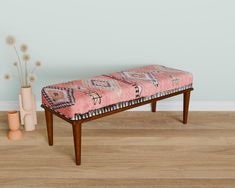 a pink bench sitting on top of a wooden floor next to a vase with flowers