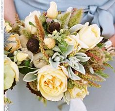 a bridal bouquet with yellow flowers and greenery is held by a woman in a blue dress