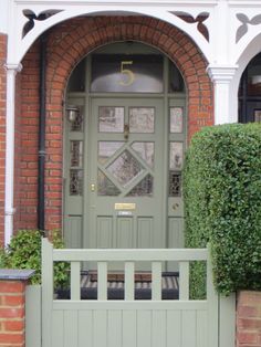 a green front door with a bench in the foreground and bushes on either side