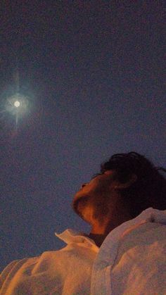 a person laying in bed with the moon behind them and blue sky above their head