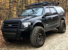 a black truck parked on top of a dirt road in front of trees and leaves