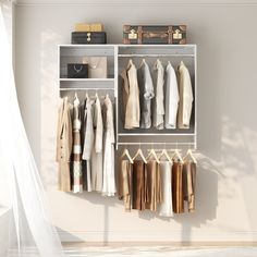 an organized closet with clothes and suitcases hanging on the wall next to a bed