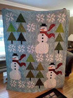 a quilted snowman is hanging on the wall in front of a window with christmas trees