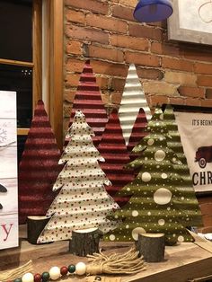 three christmas trees are on display in front of a brick wall and some other decorations