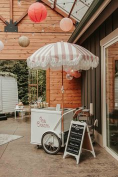 an ice cream cart with umbrellas on the outside of a building next to a sign