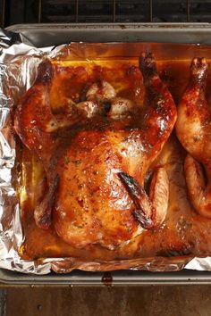 two whole chickens sitting on top of tin foil in an oven with one being cooked