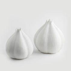 two white vases sitting next to each other on a white surface, one is shaped like an onion