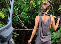 a woman in grey dress standing next to a car and holding an object up to her face