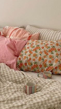 an unmade bed with pink and orange pillows, coffee cups and blankets on it