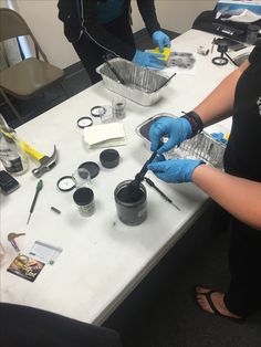 two people in blue gloves are working on some plastic containers with scissors and other items around them