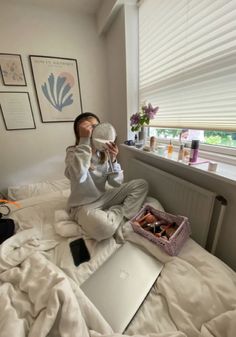 a woman is sitting on her bed drinking from a cup