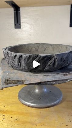 a stone bowl sitting on top of a wooden table next to a metal plate with an arrow