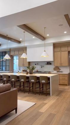 a large open concept kitchen and living room with wood flooring, white counter tops and bar stools