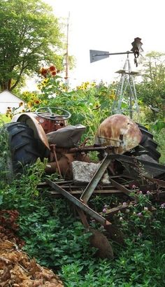 an old tractor sitting in the middle of a field next to some flowers and trees