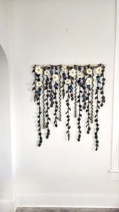 a wall hanging made out of beads and flowers on the side of a white wall