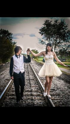 a man and woman are walking down the railroad tracks, one is holding his hand