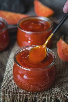 a person holding a spoon in a jar filled with sauce and slices of watermelon