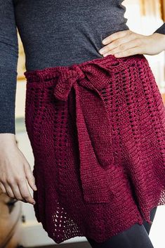 a woman is wearing a red crocheted skirt with a bow at the waist