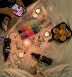 a person laying on a bed holding a cell phone and surrounded by other items that include candles