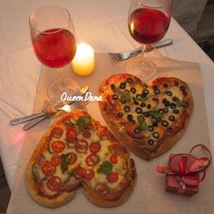 two heart shaped pizzas sitting on top of a table next to glasses of wine