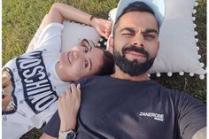 a man and woman laying on the grass with their arms around each other, looking at the camera