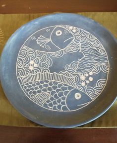 a blue plate with fish on it sitting on a wooden table next to a fan