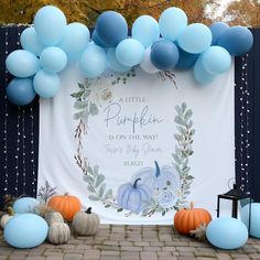 a blue and white baby shower backdrop with balloons on the ground, pumpkins in front of it