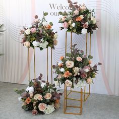 two gold stands with flowers on them in front of a welcome sign